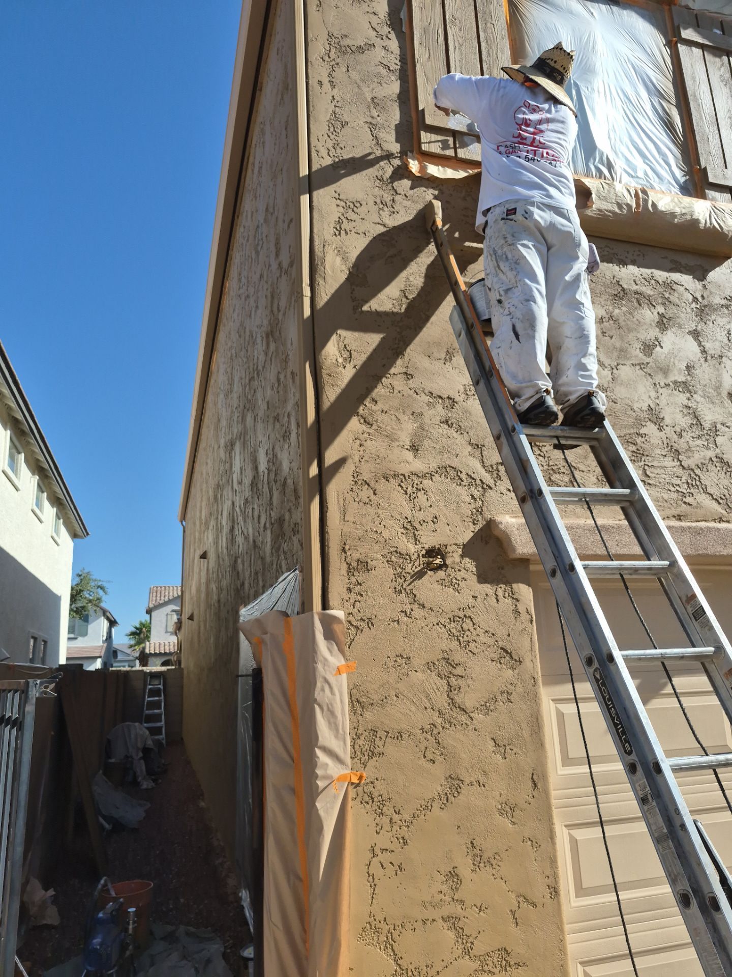 Crash of Rhinos employee on a ladder painting a masked Glendale stucco wall