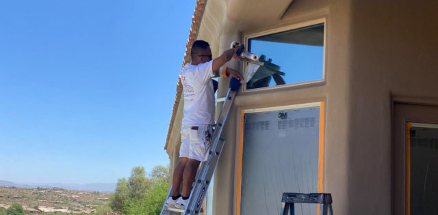 Standing on a ladder, our painter begins masking for paint in Phoenix, AZ, ensuring the windows are fully protected.