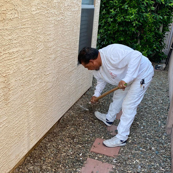Our painter uses a rake to pull landscaping rocks away from the stem wall of the home, allowing us to access it for prep and paint.